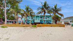 Un bungalow situé en bord de mer, doté de plusieurs pièces, d’une terrasse en bois et de palmiers.