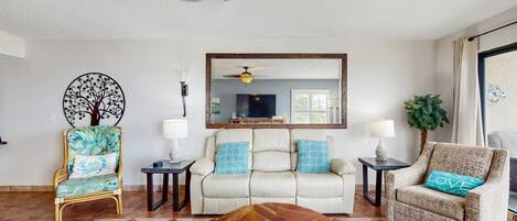 Una sala de estar con un sofá, dos sillones, una mesa de centro, un televisor y un ventilador de techo.