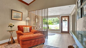A modern living room with a large orange sofa, a glass coffee table, and a patterned rug. There is a large window with a view of greenery outside. - Riverfront retreat with pool spa outdoor kitchen firepit dock sauna and games (Tampa)
