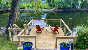 A wooden deck with two chairs and a small table, overlooking a calm body of water. - Riverfront retreat with pool spa outdoor kitchen firepit dock sauna and games (Tampa)