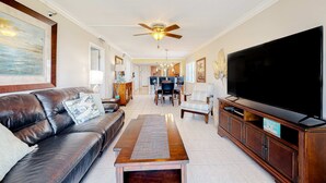 A living room with a leather sofa, a wooden coffee table, a TV on a wooden stand, a ceiling fan, and a dining area in the background. - Waterfront condo with heated pool hot tub central AC and WD snowbird friendly (Indian Shores)