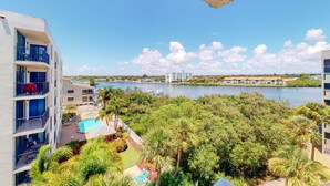 A high-rise hotel with a pool area, lush greenery, and a view of a body of water. - Waterfront condo with heated pool hot tub central AC and WD snowbird friendly (Indian Shores)