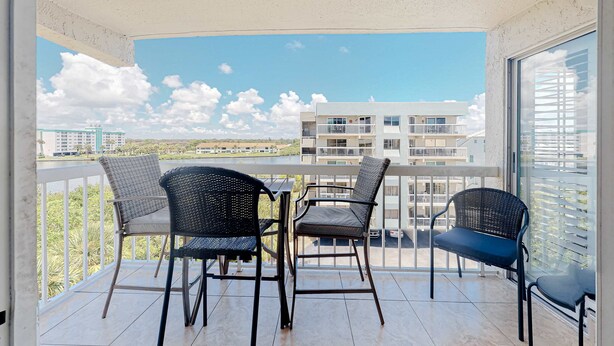 A balcony with a table and four chairs, overlooking a building and a distant landscape. - Waterfront condo with heated pool hot tub central AC and WD snowbird friendly (Indian Shores)
