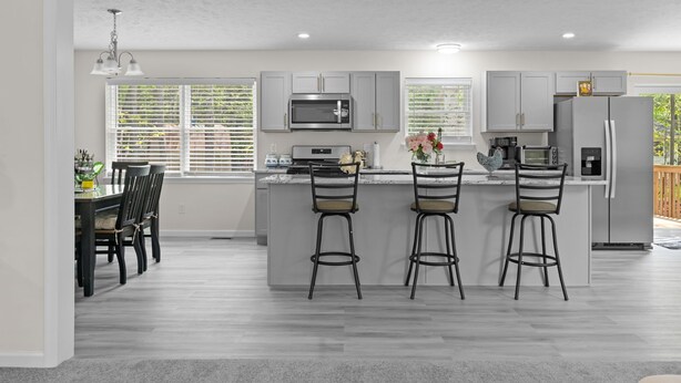 A modern kitchen with grey cabinets, a central island with bar stools, a microwave, a refrigerator, and a dining area with a table and chairs. - Large house in pleasant Poconos with HotTub PAC-MAN, Fooseball, PingPong & More! (tobyhana)