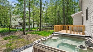 A hot tub in a backyard with a wooden deck, surrounded by trees and a house in the background. - Large house in pleasant Poconos with HotTub PAC-MAN, Fooseball, PingPong & More! (tobyhana)