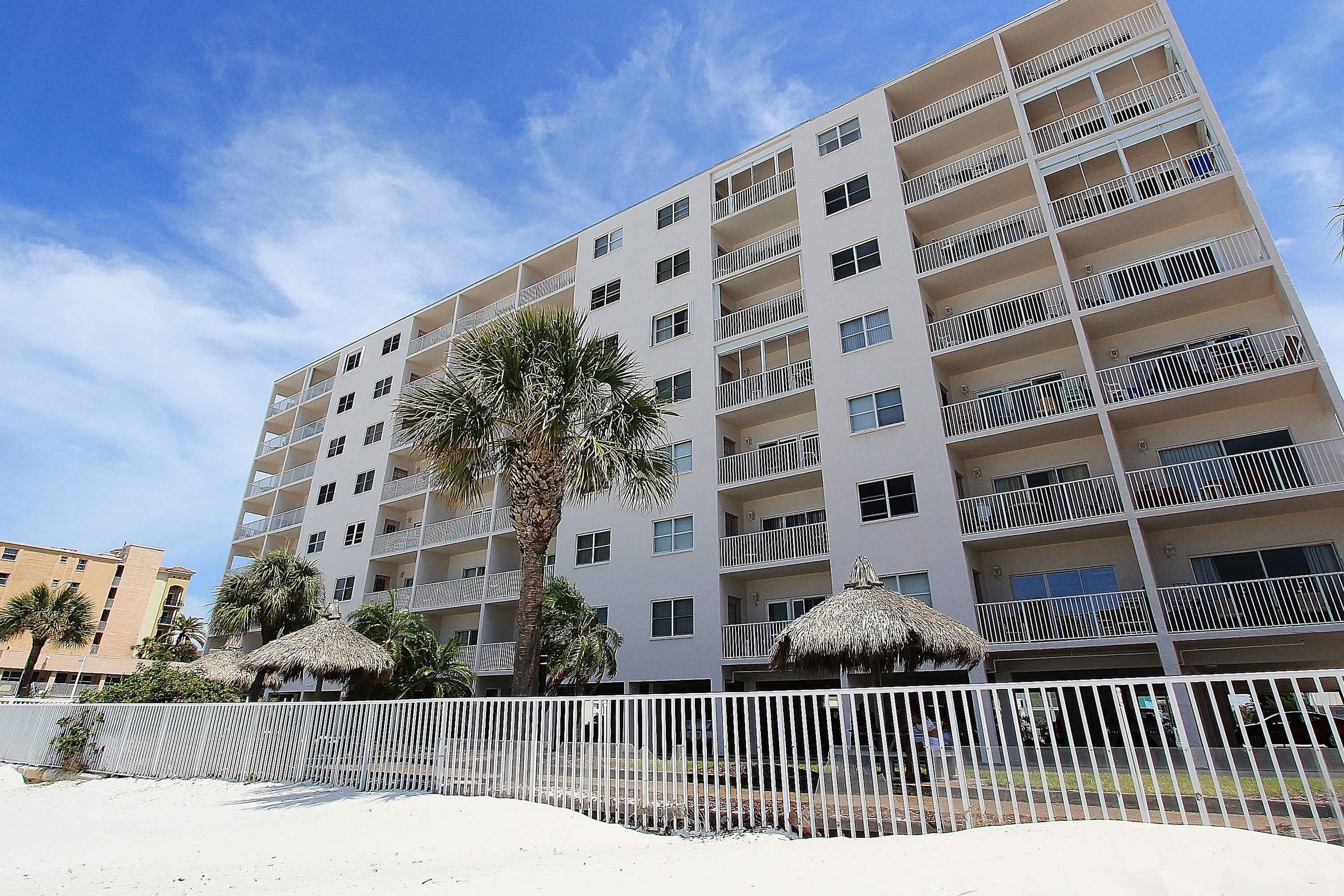 Hotel de varios pisos con balcones, una palmera y una playa al frente.