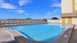 En swimmingpool med kristallklart blått vatten, omgiven av en terrass av tegel och en låg mur.