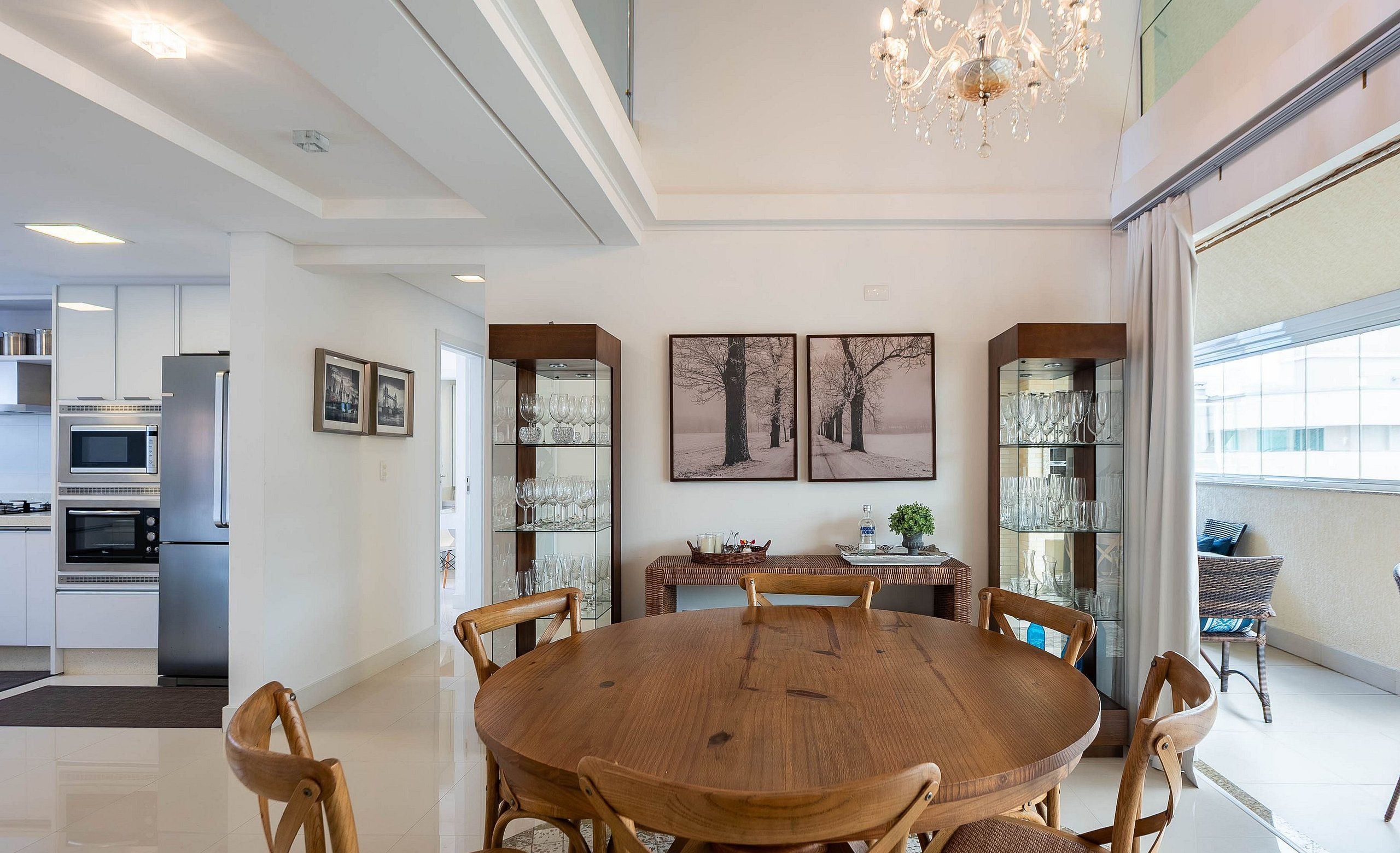 Un comedor moderno con una mesa y sillas de madera, rodeado de vitrinas con copas de vino.