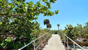 A wooden pathway with metal railings, surrounded by lush greenery and trees. - Intracoastal view condo with pool hot tub and marina access walk to beach (Madeira Beach)