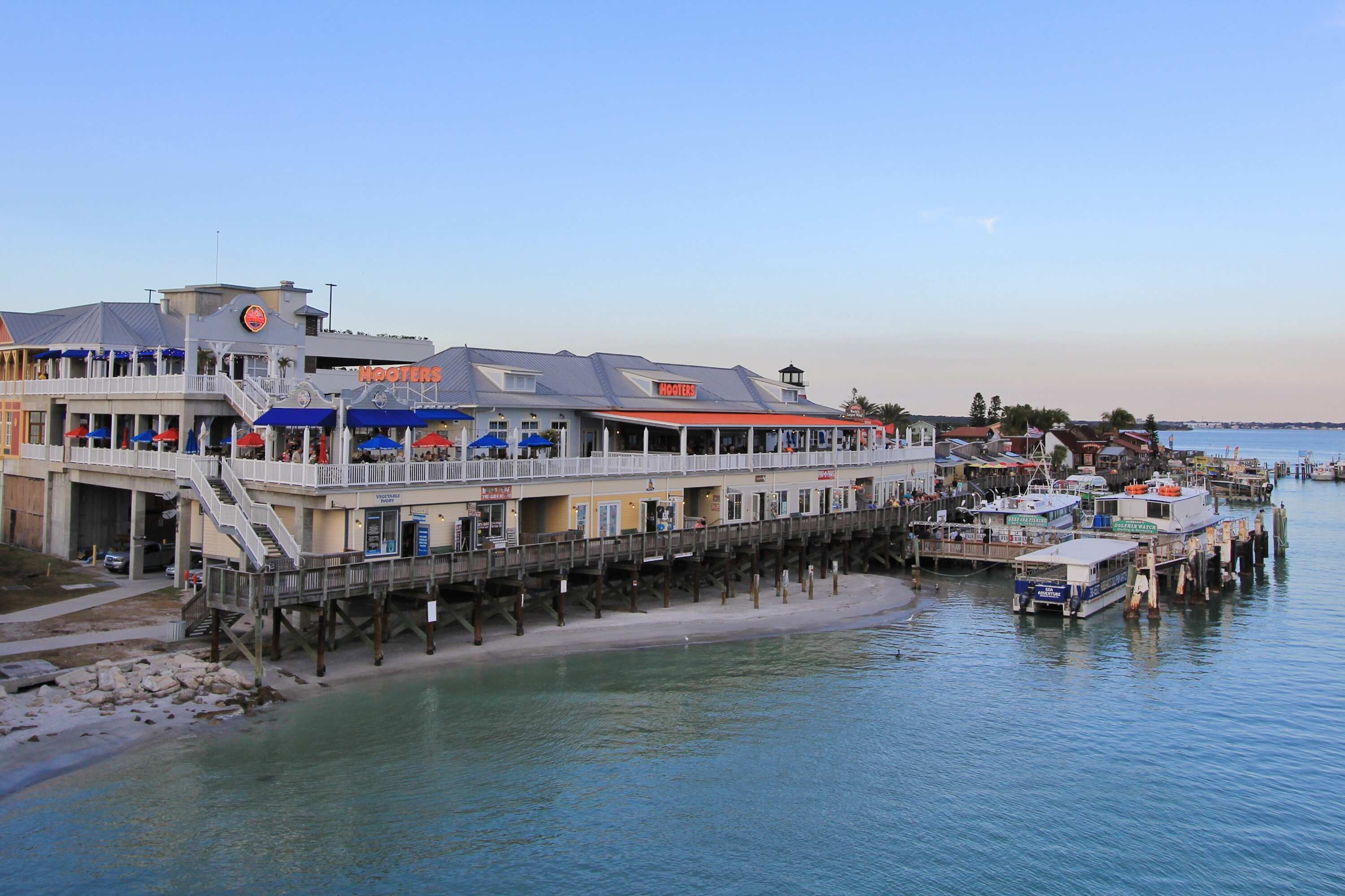 A waterfront hotel with a pier, multiple balconies, and a dock with boats.