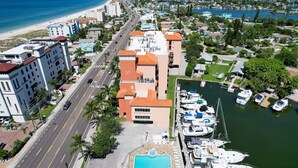 An aerial view of a coastal area with a marina, a swimming pool, and buildings with balconies overlooking the water. - Intracoastal view condo with pool hot tub and marina access walk to beach (Madeira Beach)