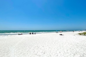 Uma extensa praia de areia com céu azul límpido e mar calmo.