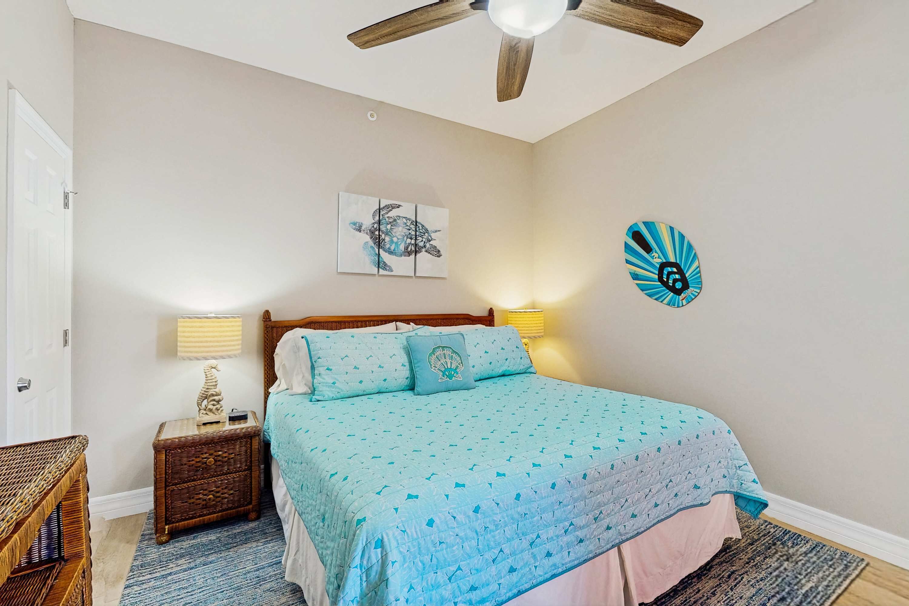 A bedroom with a bed, a ceiling fan, a wall-mounted lamp, a decorative plate, and a framed picture.