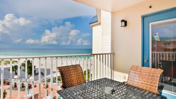A balcony with a view of the beach and ocean, a table with chairs, and a door with a blue frame.