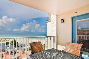 A balcony with a view of the beach and ocean, a table with chairs, and a door with a blue frame. - 4th floor beachfront corner condo with private balcony views BBQ AC (Indian Shores)