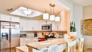 A modern kitchen with white cabinets, stainless steel appliances, a granite countertop, and pendant lighting.