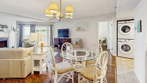 A living room with a round glass table, white chairs, a beige sofa, a chandelier, a fireplace, and a washing machine. - Charming condo with gorgeous Gulf views and beachfront heated pool and spa (Indian Shores)