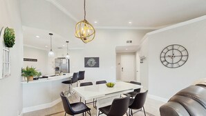 Un comedor moderno con una mesa blanca, sillas negras y un lujoso aplique.