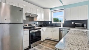 A modern kitchen with white cabinets, stainless steel appliances, and a granite countertop. - Coral Cottage House in Pine Island (Weeki Wachee)