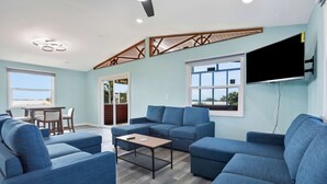 A modern living room with blue sofas, a wooden coffee table, and a flat-screen TV mounted on the wall. - Coral Cottage House in Pine Island (Weeki Wachee)