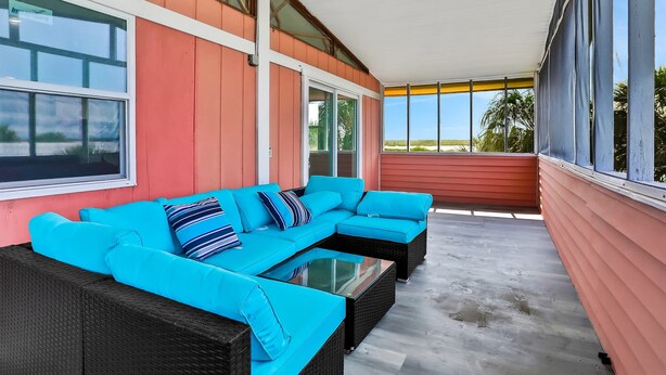A covered outdoor seating area with a bright blue sofa and a glass-top table. - Coral Cottage House in Pine Island (Weeki Wachee)