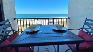 Ein Tisch mit zwei Schalen und zwei Weingläsern auf einem Balkon mit Blick auf den Strand.