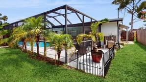 Une maison moderne dotée d’un patio couvert, d’une piscine et de palmiers.