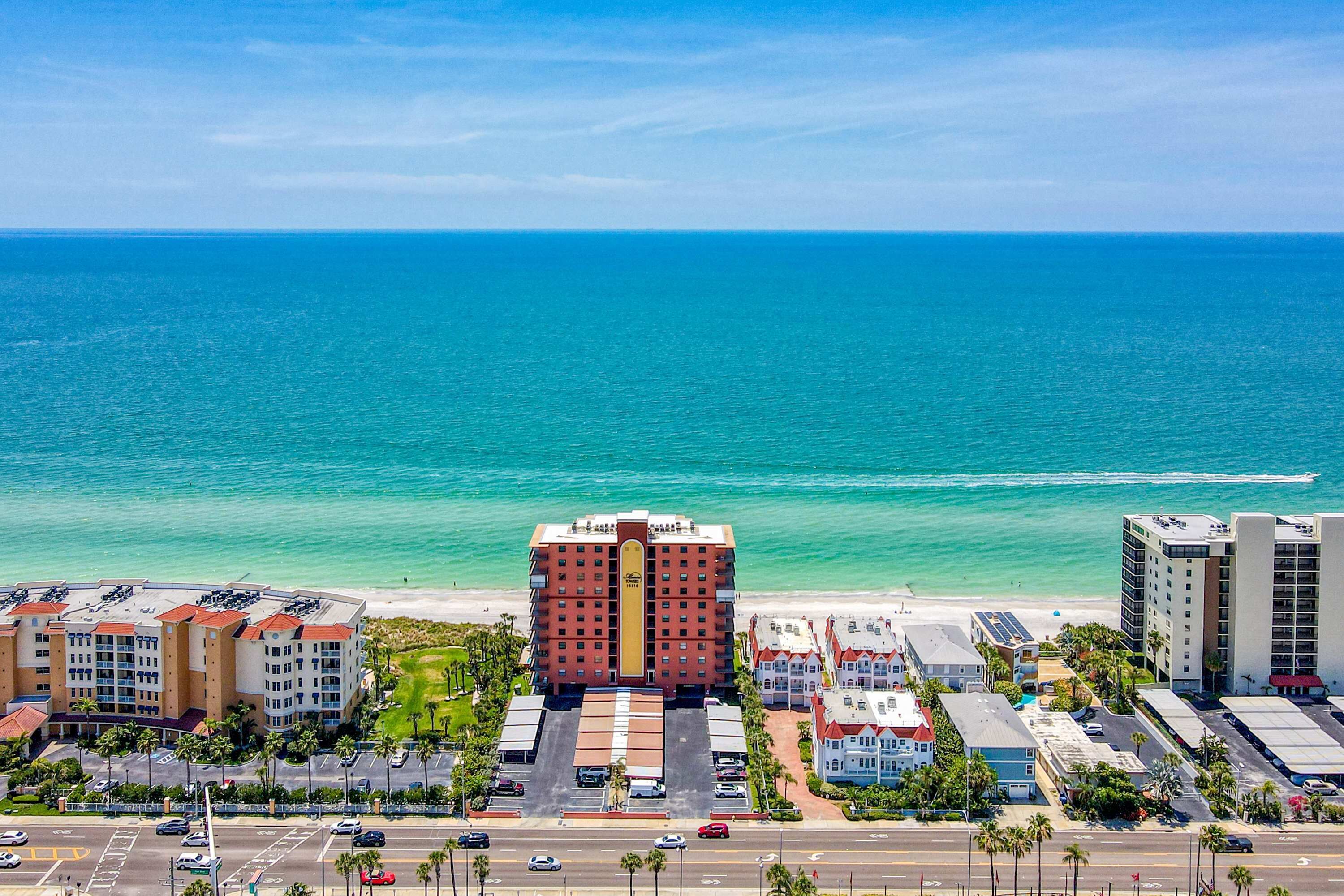 Un hôtel situé sur la côte, doté d’un bâtiment principal, d’un parking et offrant une vue sur la plage.