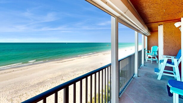 Blick auf den Strand von einem überdachten Balkon mit Stühlen und Geländer.