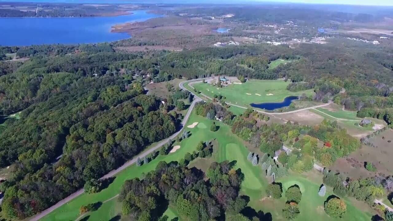 Vue aérienne d’un terrain de golf avec un lac, entouré d’une forêt dense.