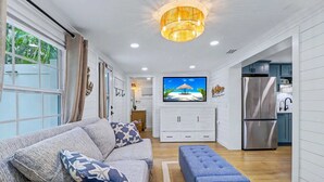 A modern living room with a sofa, ottoman, and a television displaying a beach scene.