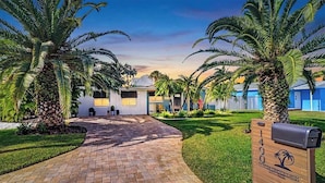 A pathway leading to a building with a brick entrance, surrounded by palm trees and a well-maintained lawn.