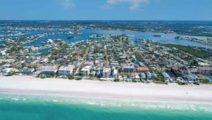 An aerial view of a coastal residential area with a beachfront, numerous buildings, and a marina.