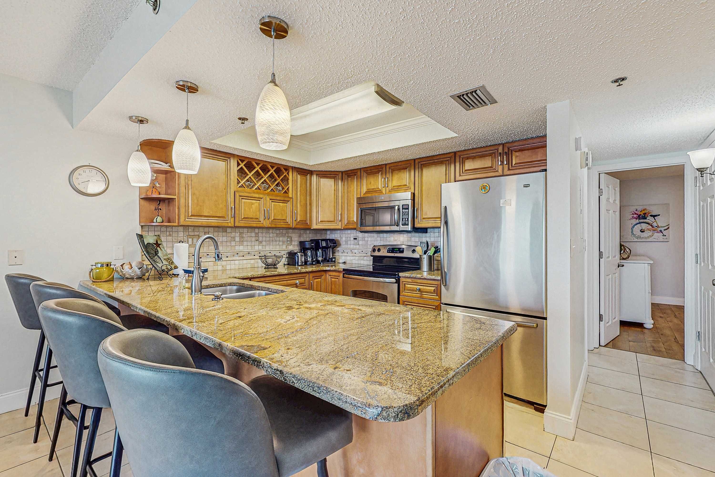 A kitchen with granite countertops, stainless steel appliances, wooden cabinets, and pendant lighting.