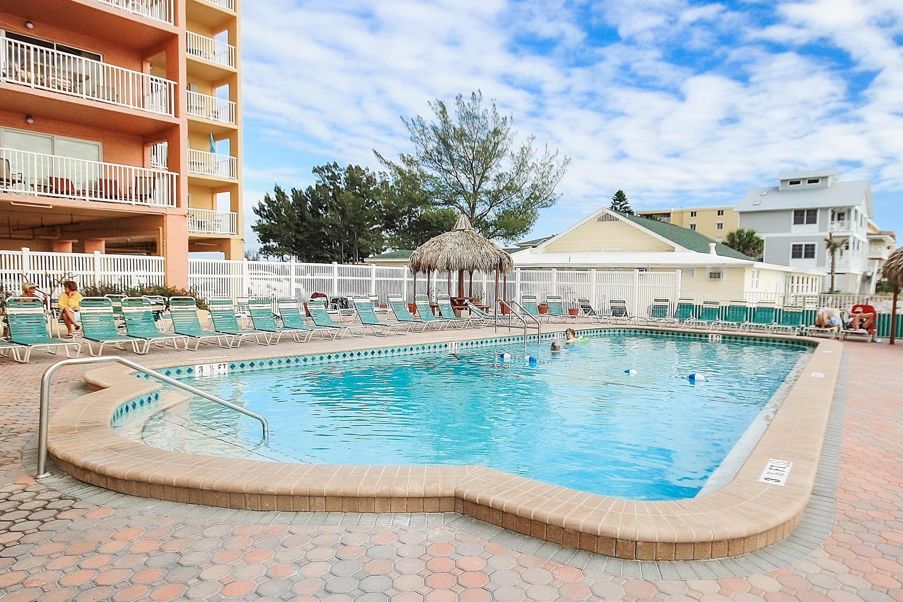 A rectangular swimming pool with a tiled deck, surrounded by lounge chairs and a white fence.