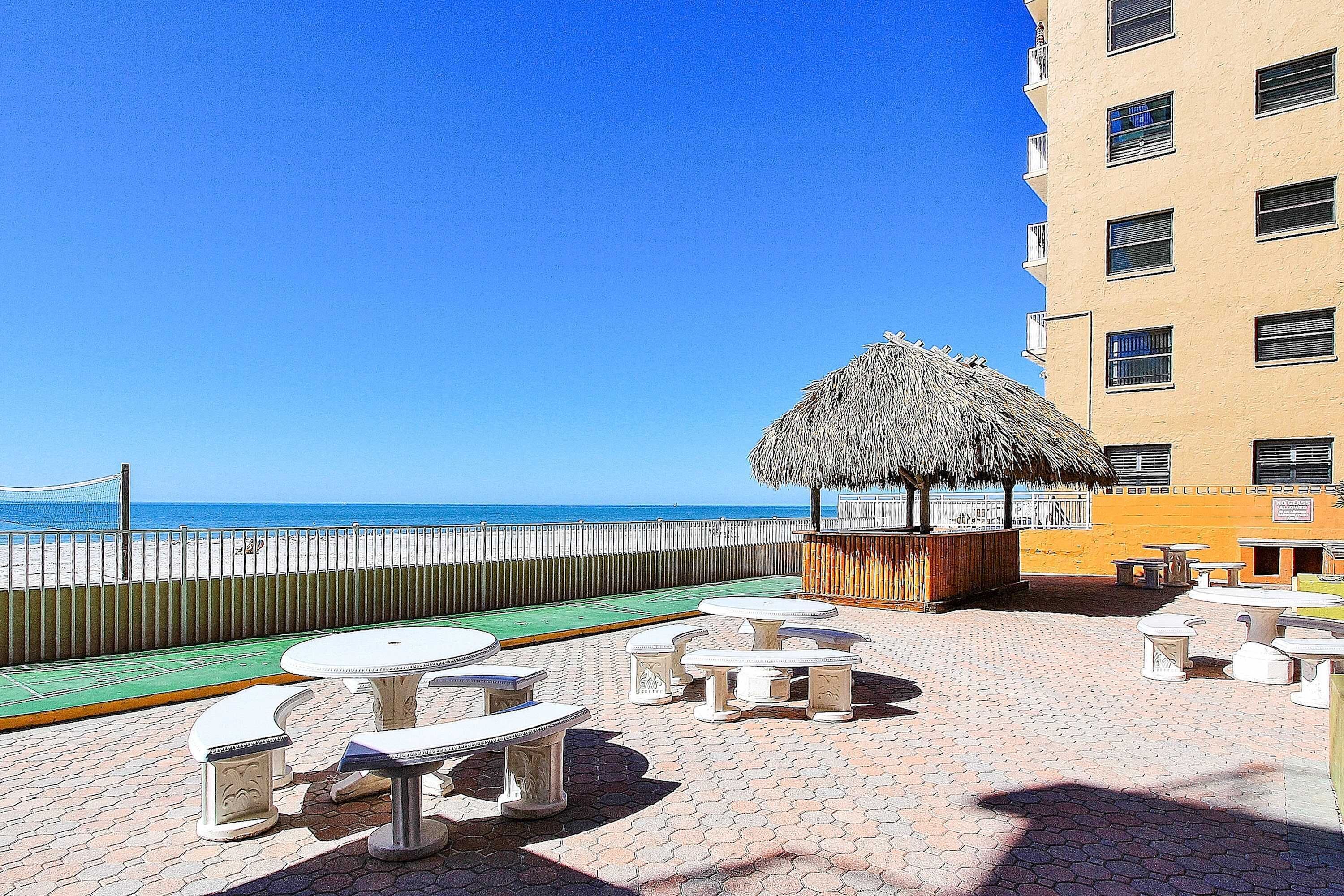 Eine Terrasse direkt am Strand mit Tischen und Stühlen, einem Reetdachschirm und Blick auf das Meer.
