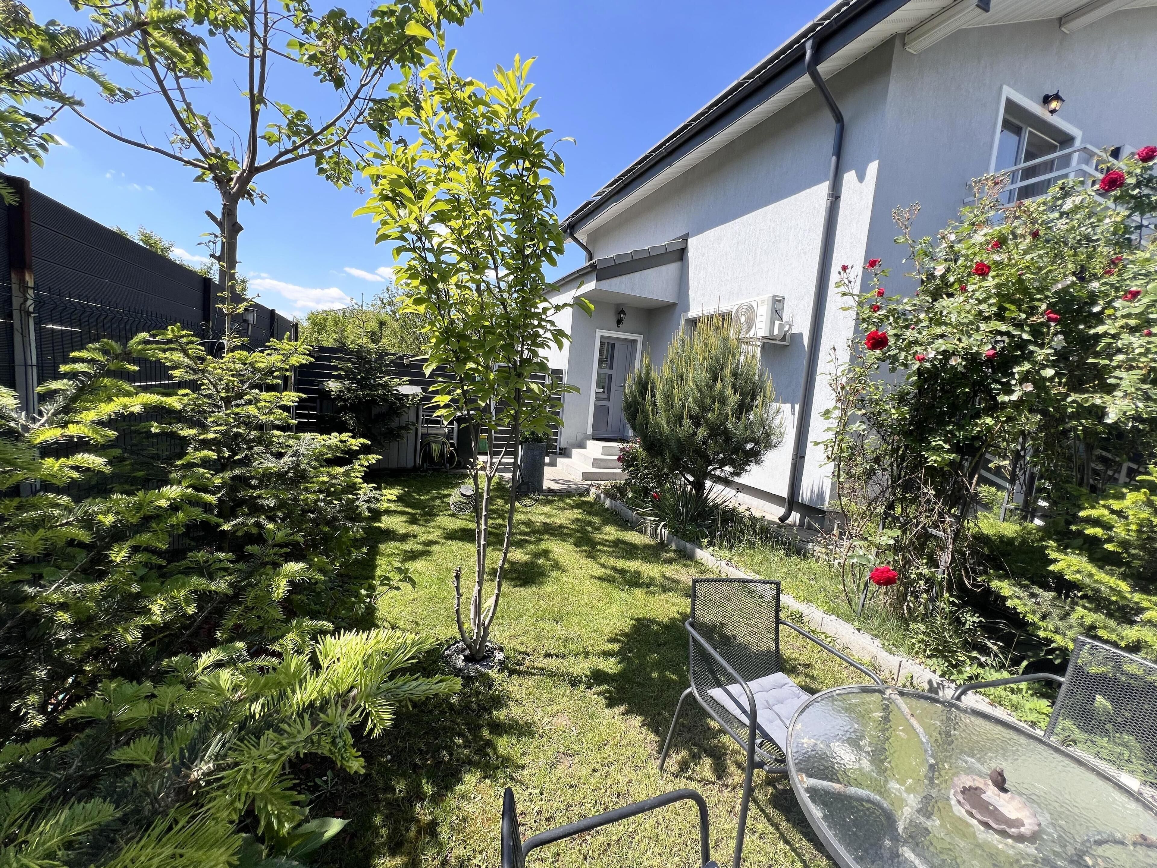 A well-maintained garden with various plants and a glass table with chairs.