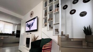 A modern living room with a flat-screen TV, a green armchair, a staircase, and decorative wall art. - Villagrey Residence Tunari (Tunari)