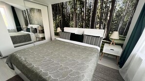 A modern bedroom with a large bed, a nightstand, a mirror, and a view of a forest through the window. - Villagrey Residence Tunari (Tunari)