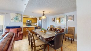 A spacious living area with a sofa, dining table, and chairs. A kitchen is visible in the background.