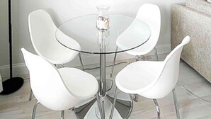 Een ronde glazen tafel met vier witte stoelen.