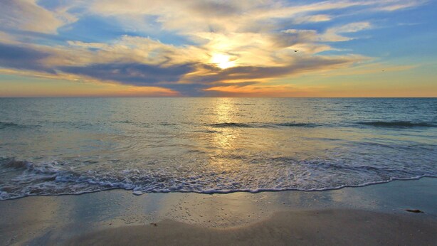 Une plage où les vagues viennent doucement lécher le rivage sous un ciel embrasé par le coucher de soleil.
