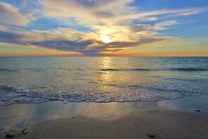 Une plage où les vagues viennent doucement lécher le rivage sous un ciel embrasé par le coucher de soleil.