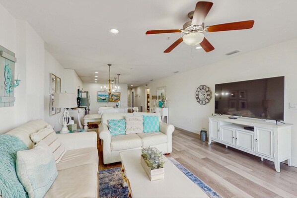A living room with a white sofa, a coffee table, a TV, and a ceiling fan. - Beach chic condo across from beach close to John s Pass on site pool dogs ok (Madeira Beach)