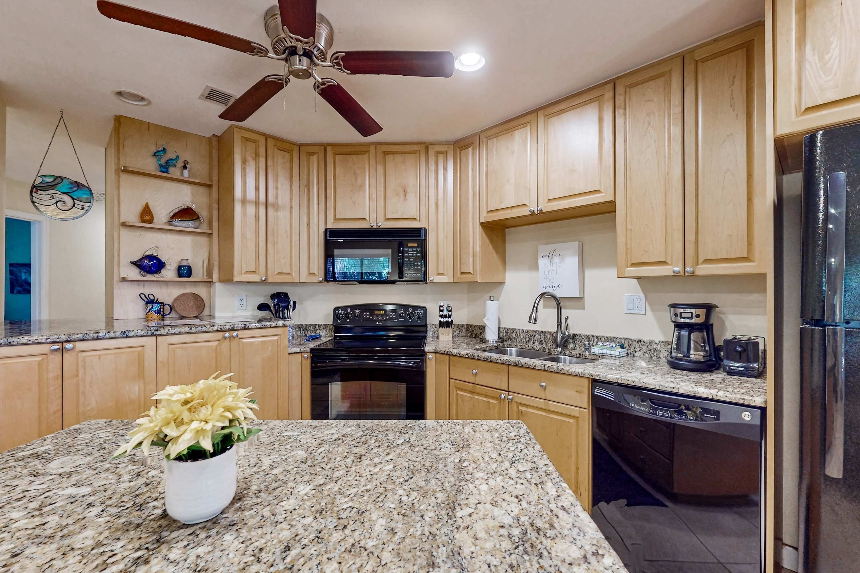 A kitchen with wooden cabinets, granite countertops, a ceiling fan, a microwave, a stove, a dishwasher, and a refrigerator.