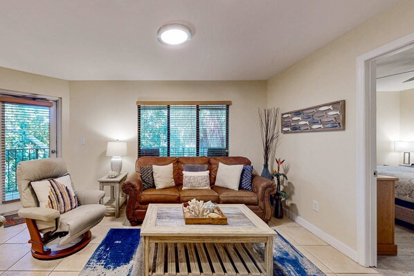 Una sala de estar con un sofá de cuero marrón, un sillón color beige, una mesa de centro de madera y un tapete azul.