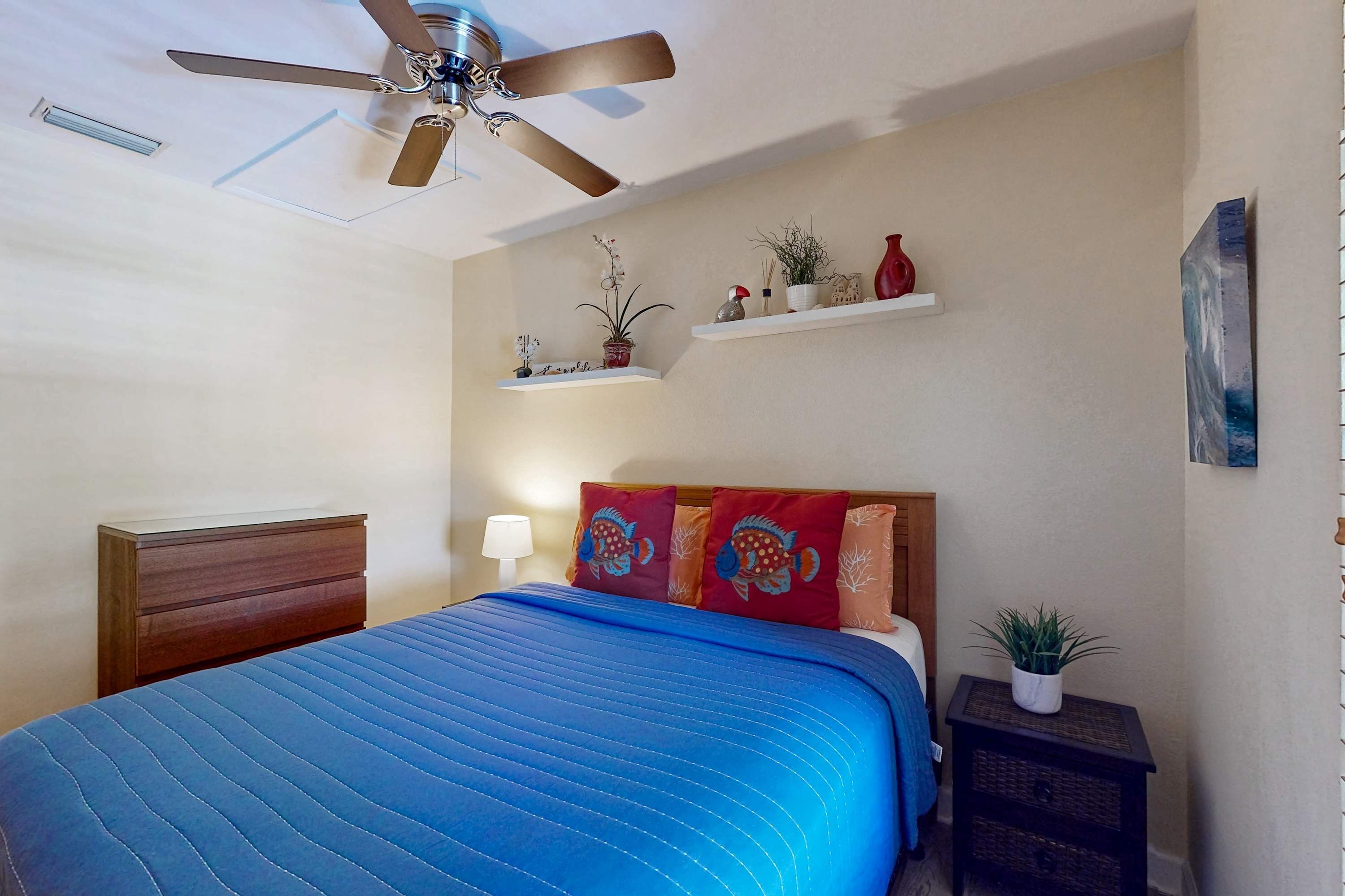 A bedroom with a bed, a ceiling fan, a nightstand, a dresser, and wall-mounted shelves with decorative items.