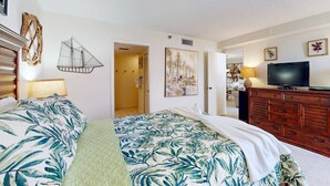 A hotel room with a bed, a TV, a dresser, and a door leading to another room. - Waterfront condo with pool and spa directly across from wide beach (Indian Shores)