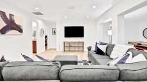 Un salon moderne avec un canapé gris, un téléviseur à écran plat fixé au mur et un meuble de rangement en bois.