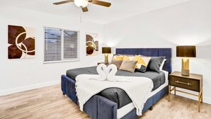 Une chambre à coucher avec un lit, des tables de chevet, un ventilateur de plafond et des œuvres d’art accrochées aux murs.
